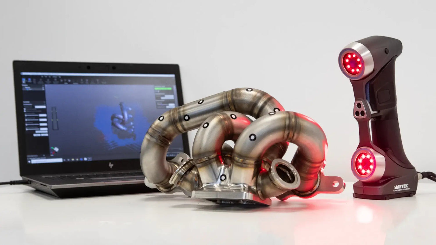 Desk shot showcasing a high-performance manifold alongside advanced modelling and scanning technology used in Nortech Performance's engineering processes.