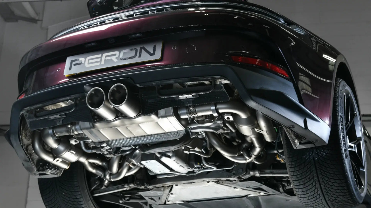 Porsche 992 GT3 Touring on a lift ramp post-Akrapovic performance exhaust installation, showcasing titanium craftsmanship and precision engineering.