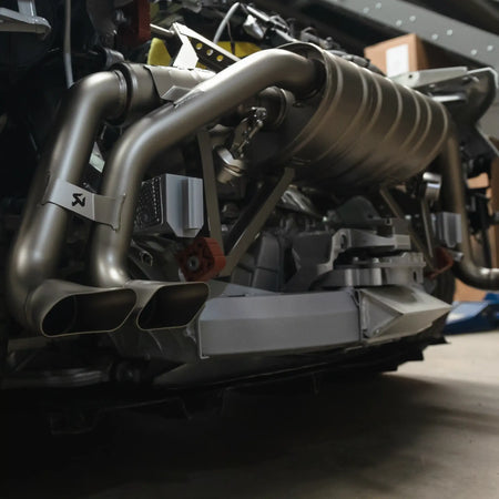 The Akrapovič Slip-On Line exhaust system installed on an Audi R8 in PERON's Performance Workshop, captured with the rear bumper removed to showcase the intricate titanium construction and dual-mode valve system.