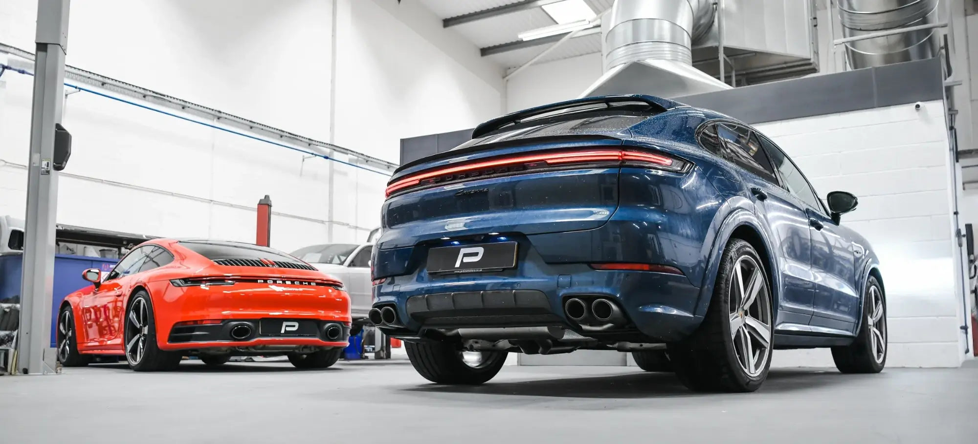 Porsche Cayenne 536.2 and Porsche 992 Carrera parked in the performance workshop after Akrapovič exhaust installations, showcasing precision craftsmanship.