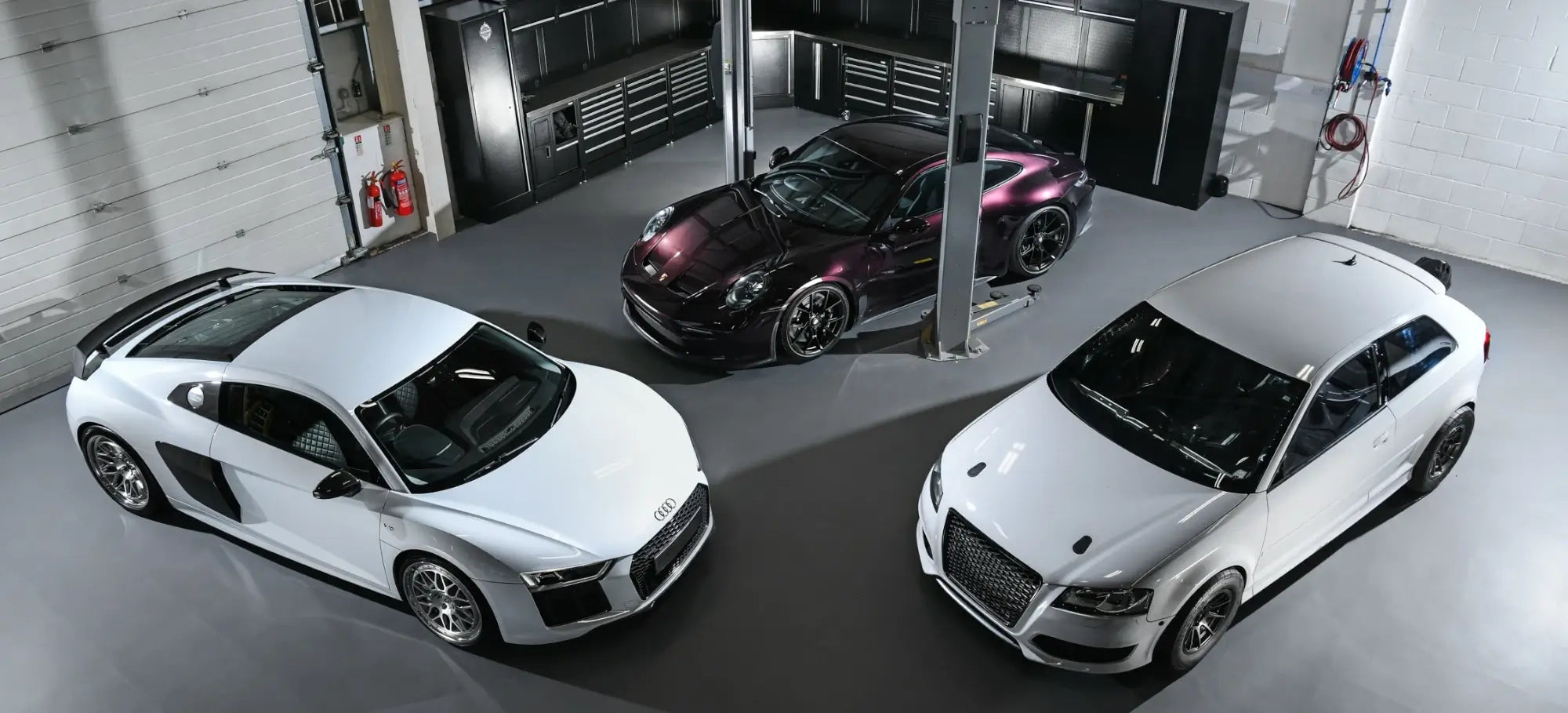 Group shot of Audi R8, Porsche 992 GT3 Touring, and Audi S3 8P project car parked in PERON's Performance Workshop, showcasing state-of-the-art facilities.