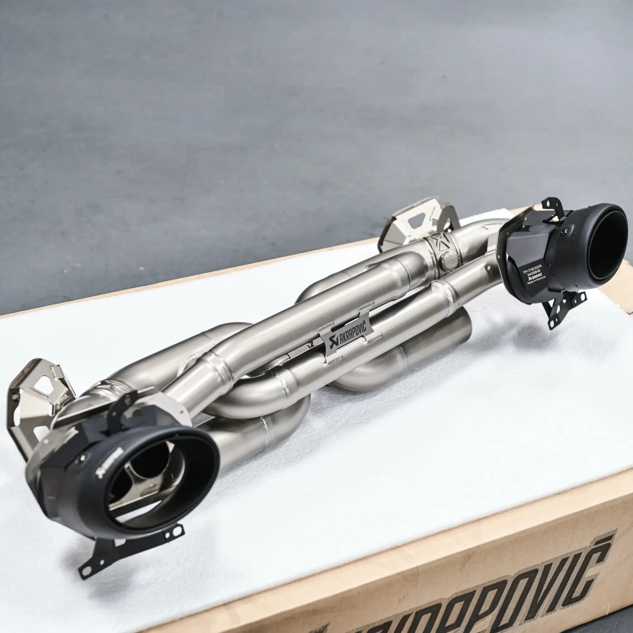 Akrapovič Slip-On Race Line (Titanium) performance exhaust system displayed on its Akrapovič packaging, prior to installation on a Porsche 911 Turbo S 992.1.